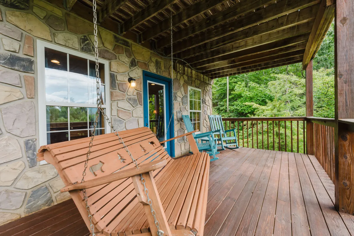 A peaceful porch scene with a swinging bench, blue door, and a green rocking chair, evoking the feeling of enjoying fresh air, scenic views, and the sounds of the outdoors. The setting suggests a quiet spot to rest, observe wildlife, or reflect on the day's adventures.