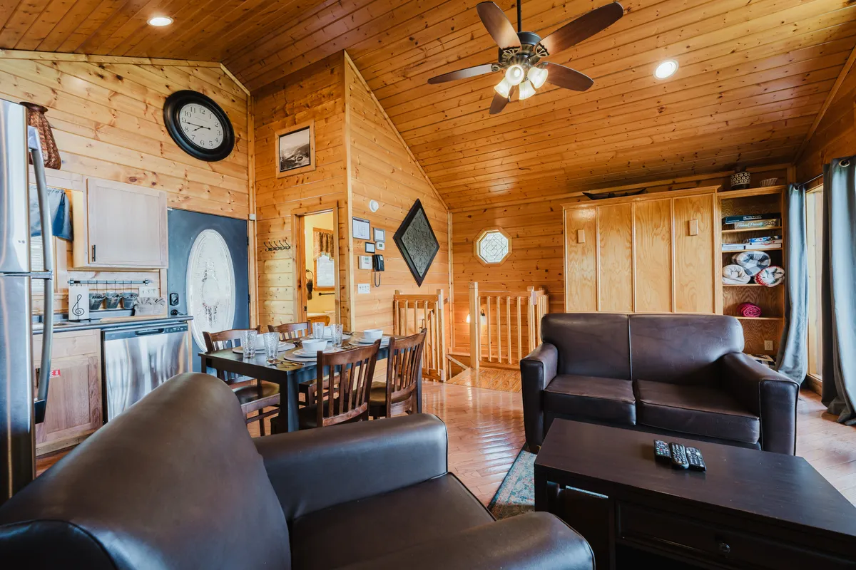 A spacious open-plan area with a wooden ceiling, a dining table with chairs, comfortable sofas, and an adjacent kitchen. The layout encourages group gatherings, shared meals, and casual lounging.