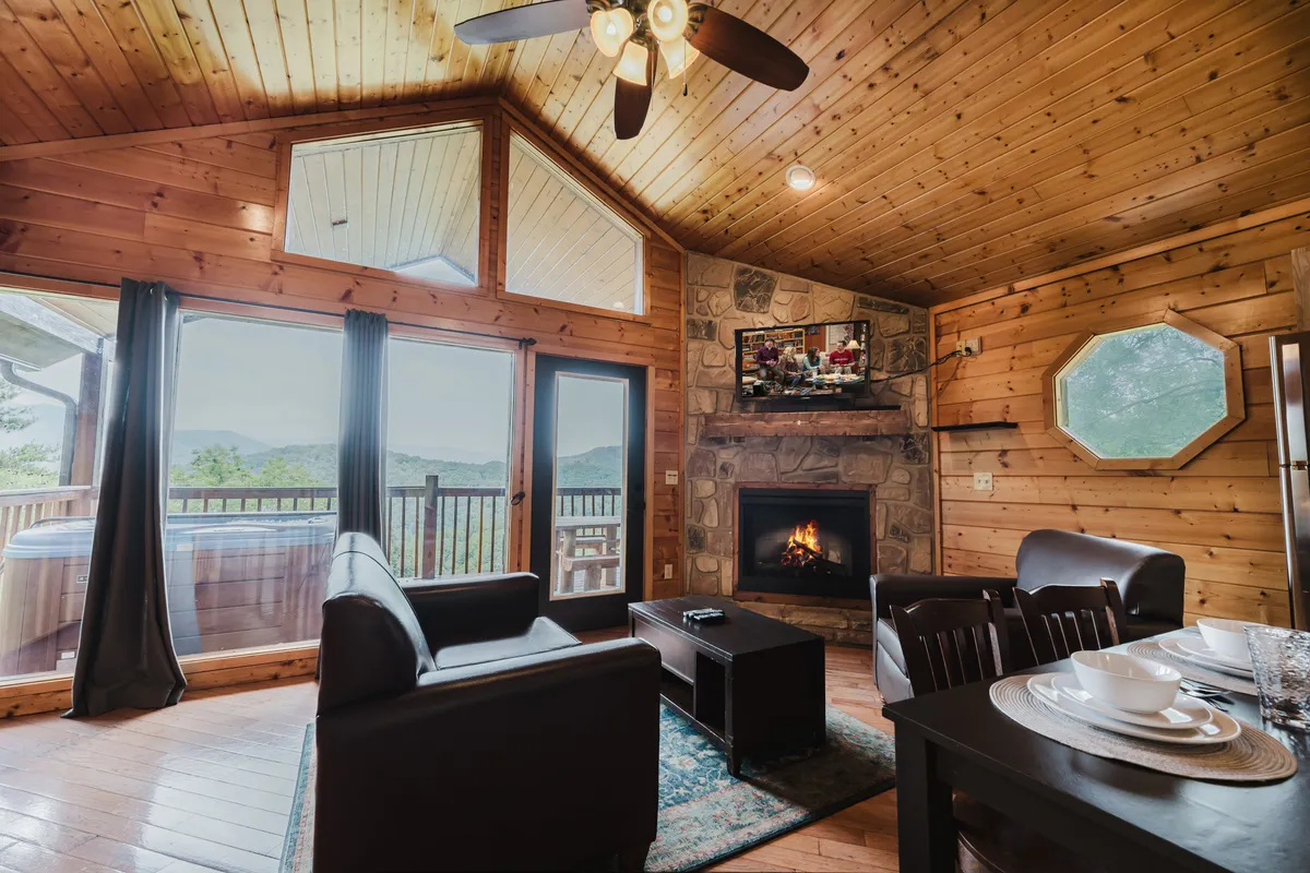 A welcoming interior featuring a fireplace, large windows framing the outdoors, wooden furniture, and a hot tub visible through the glass doors. The mood is warm and inviting, evoking both social gatherings and tranquil relaxation.
