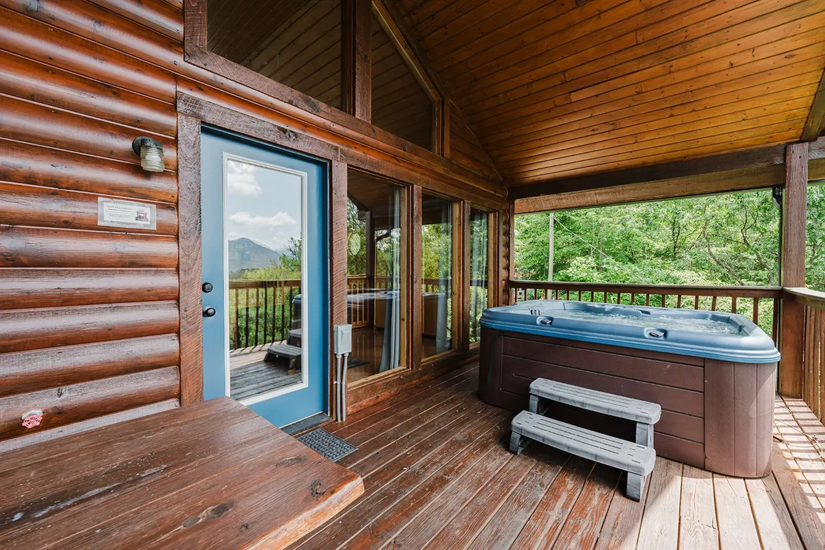 A spacious wooden deck featuring a hot tub, seating area, and large windows framing majestic mountain views. The setup suggests relaxation after an active day, with ample space for gathering and enjoying the scenery together.
