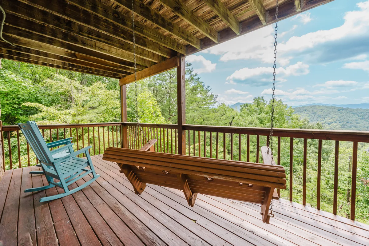 A peaceful porch scene with a swing bench, rocking chair, and lush greenery set against a stunning mountain backdrop. The space feels serene and perfect for unwinding or enjoying quiet family moments while soaking up the scenery.