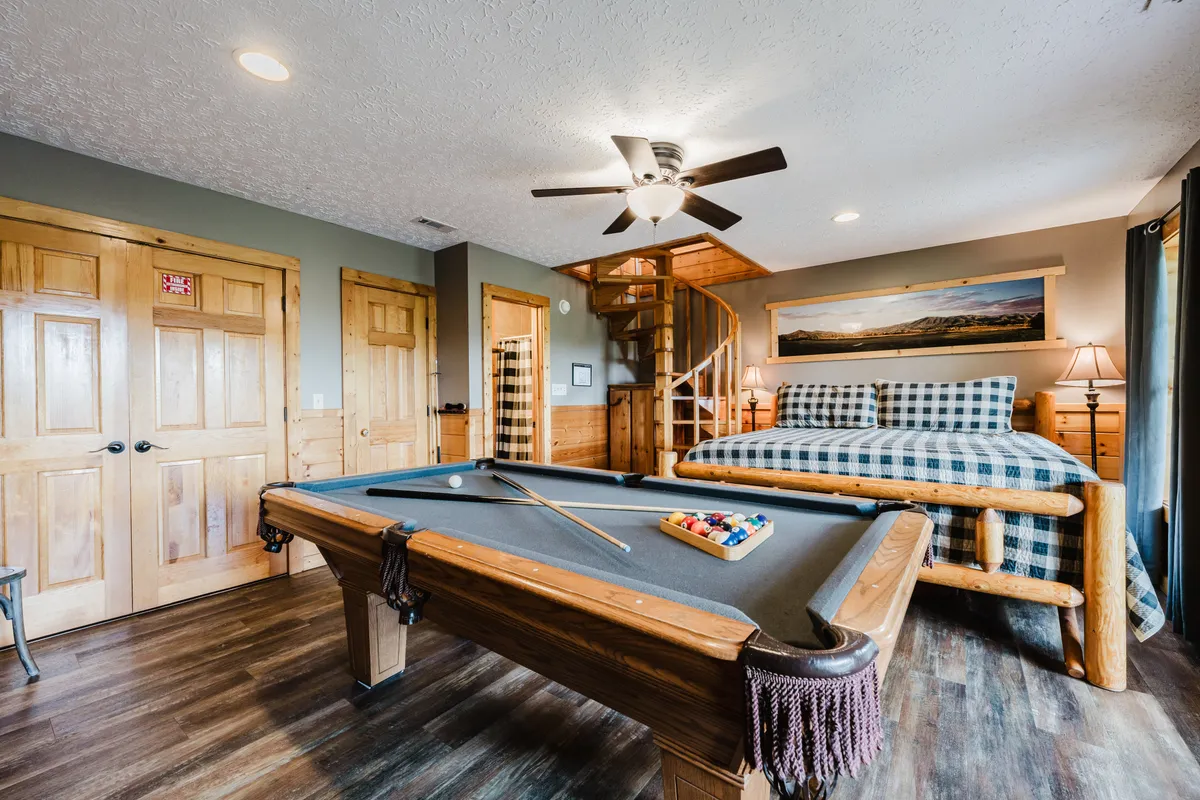 A playful and comfortable space featuring a pool table, a cozy bed, a spiral staircase, and rustic wooden doors. The area invites socializing, playing games, and unwinding after exploring local attractions.