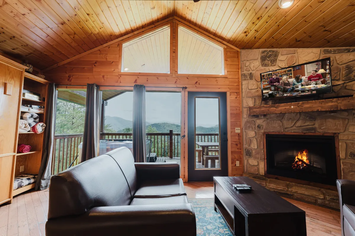 A warm and welcoming living room featuring a fireplace, a comfortable sofa, large windows with sweeping mountain views, and a television - ideal for snuggling up for a movie night or simply soaking in the scenery.