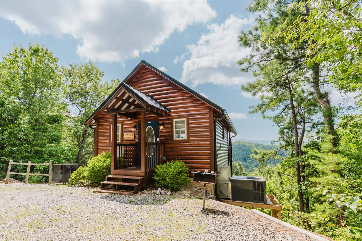 A classic log cabin stands amidst tall trees with a mountain vista in the background. The inviting front porch is the gateway to the cabin’s seclusion, surrounded by the serenity of nature and hinting at activities like hiking and stargazing.