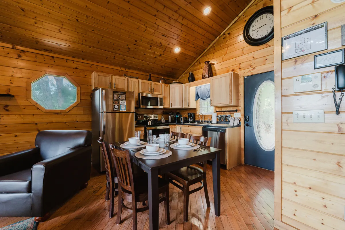 A cozy shot of the dining area and kitchen, where the dining table is set for a meal, a comfortable armchair beckons, and modern kitchen appliances are visible. The space feels intimate and perfect for enjoying hearty breakfasts or candlelit dinners with loved ones.
